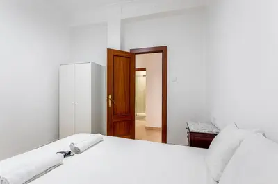 a white bedroom with a bed and a wooden door at Guest Ready - Bright flat well‑located urban stay in Valencia