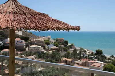 a straw umbrella on a balcony with the ocean at Cap Blanc Penthouse Cullera in Faro de Cullera