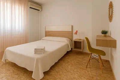 a bedroom with a white bed and a yellow chair at Rooms Avenida in Tavernes de Valldigna