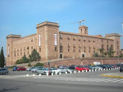 a large brick building with cars parked in a parking lot at Olympia Ronda Hostel in El Puig