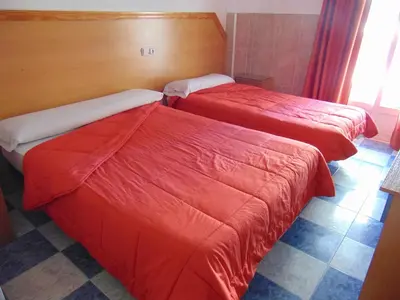 two beds in a hotel room with red sheets at Hotel Libertador in Cullera