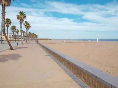 a sandy beach with palm trees and a sidewalk at ApartUP Patacona Beach II in Valencia