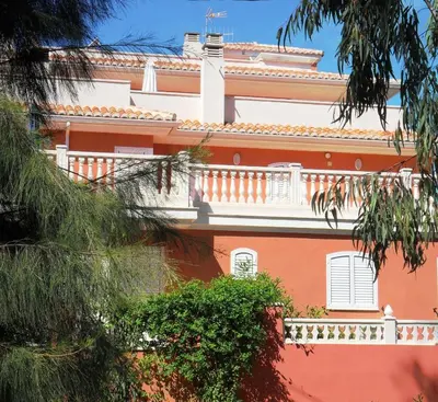 a red building with a white balcony and trees at Apartamentos Concha del Mar in Sagunto