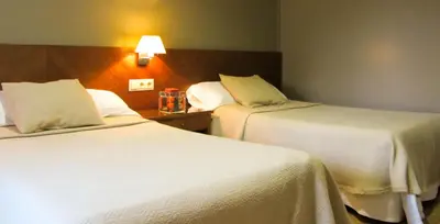 two beds in a hotel room with white sheets at Hotel Avenida in Requena