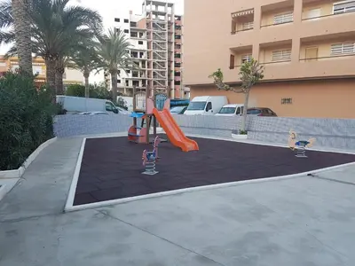a playground in a parking lot with a slide at Apartamento Barbacoa, Piscina y playa in Puebla de Farnals