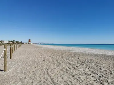 a sandy beach with a fence and the ocean at Global Vacacional, Adosado en la playa con piscina in Sagunto