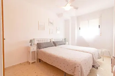a white bedroom with two beds and a window at Global Vacacional, Increíble apartamento en la playa, Canet d'en Berenguer in Canet de Berenguer