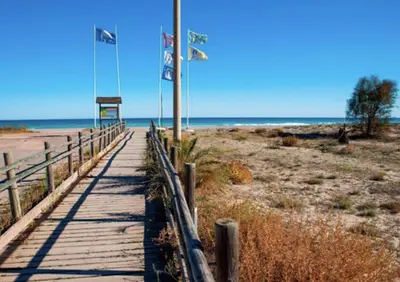 a boardwalk to the beach with flags on it at Global Vacacional, Adosado en primera linea de playa con vistas al mar in Sagunto