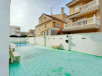 a swimming pool with two chairs and a building at Global Vacacional, apartamento cerca del mar en Canet in Canet de Berenguer