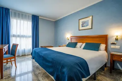 a bedroom with a large bed with blue walls and a desk at Hotel Bartos in Almussafes