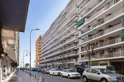 a street with cars parked in front of a large building at Levante, 6-J in Cullera