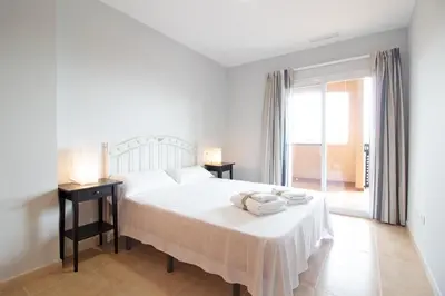a white bedroom with a bed and a window at Global Vacacional, Apartamento con terraza y piscina en la playa de Canet in Canet de Berenguer