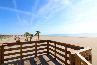 a wooden boardwalk leading to the beach with palm trees at Global Vacacional, Apartamento para 5 personas con terraza y barbacoa in Canet de Berenguer