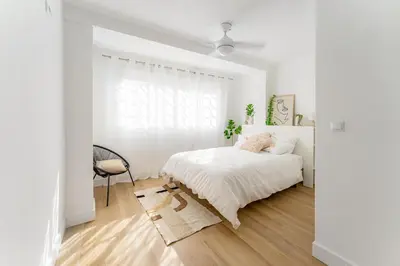 a white bedroom with a bed and a chair at Espectacular piso reformado al lado del rio Turia in Valencia